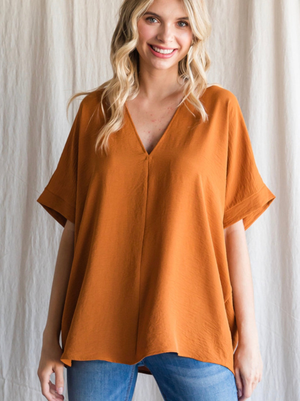 A woman wearing a caramel-colored boxy top with a V-neckline and short sleeves.