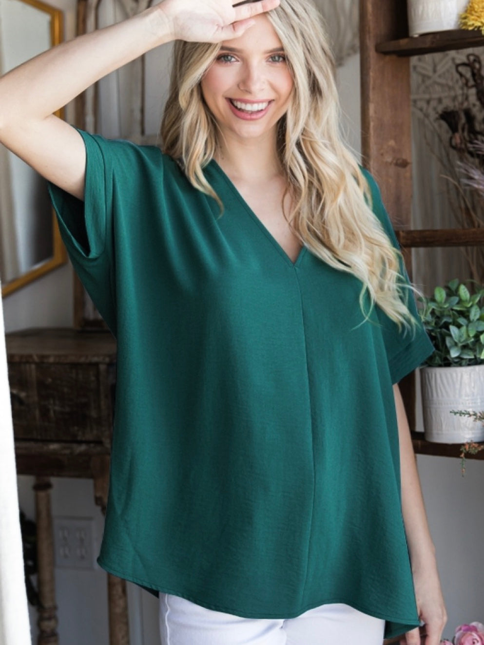 A woman wearing a hunter green, solid boxy top with a V-neckline and short sleeves.